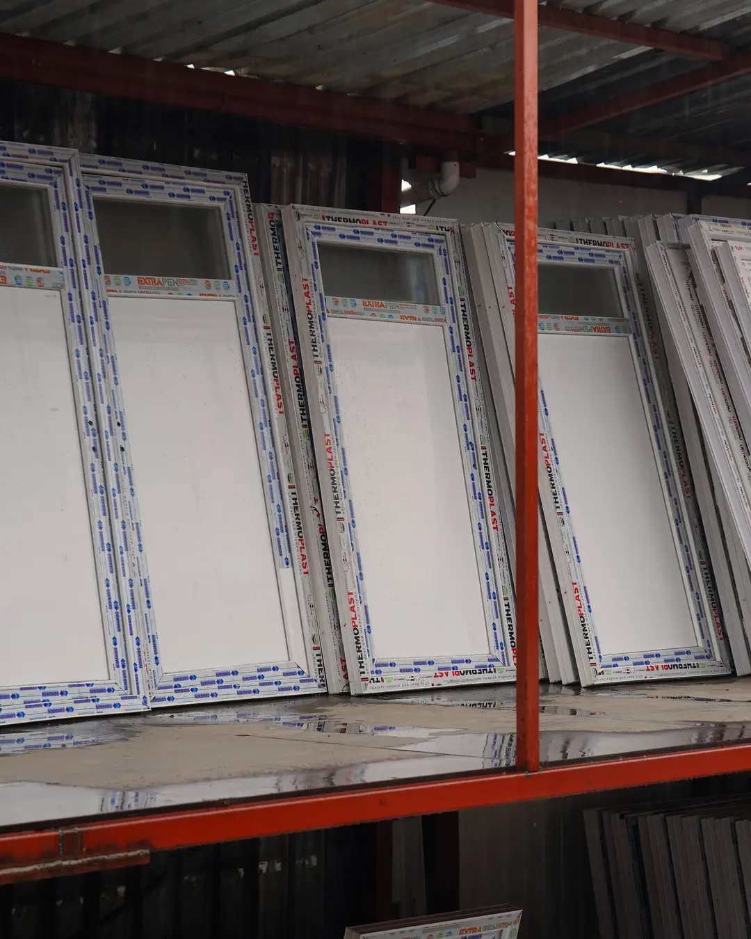 Depo raflarında dizili beyaz PVC pencere ve kapılar